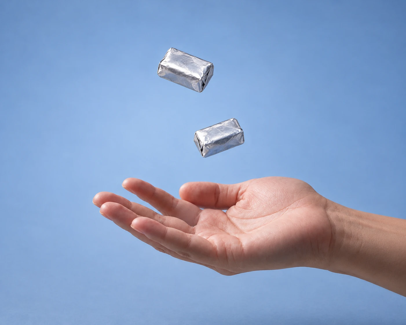 Two silver foil-wrapped chews dropping into an open hand